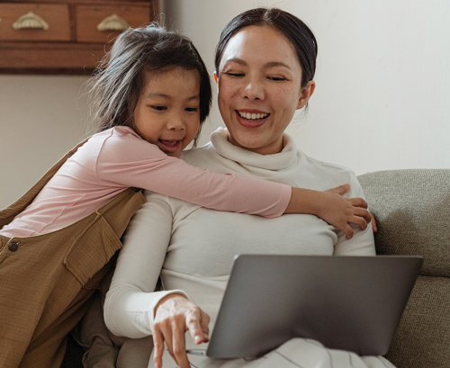 little girl hugging her mother while they look at her computer